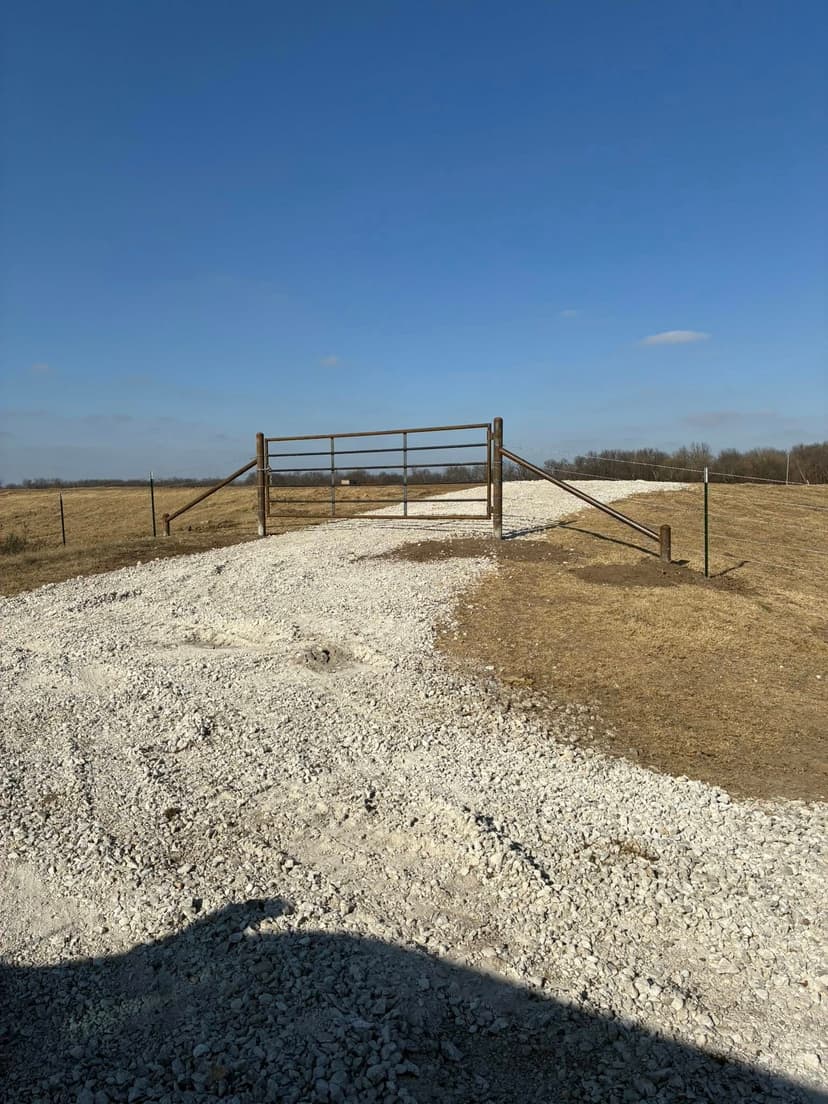 Gravel path leading to an open gate on a sunny day in a rural landscape.